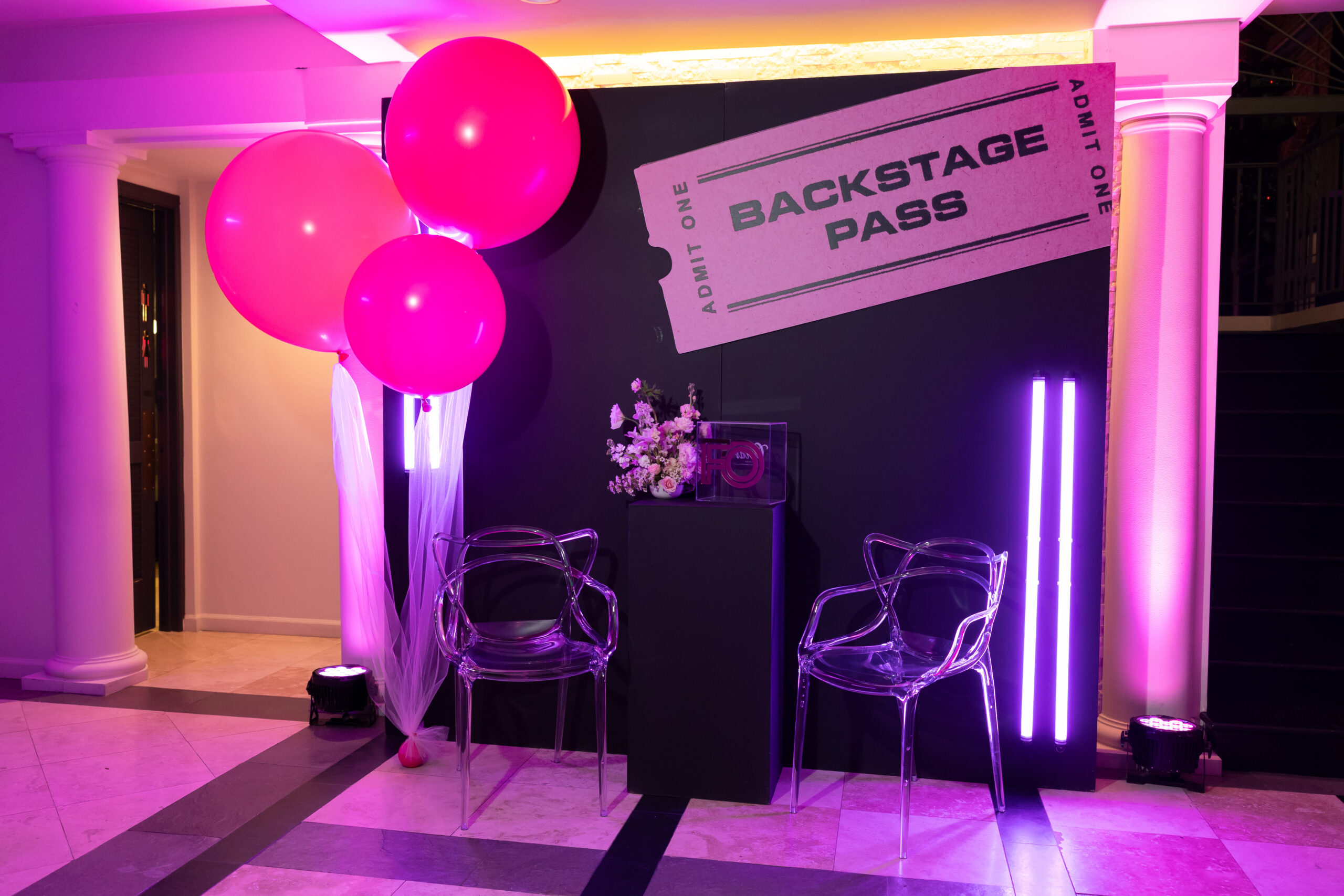 111JanBirch979A6248 - Bronson Hospitality Event backdrop with pink and purple lighting, large pink balloons, clear acrylic chairs, and a'Backstage Pass' banner.
