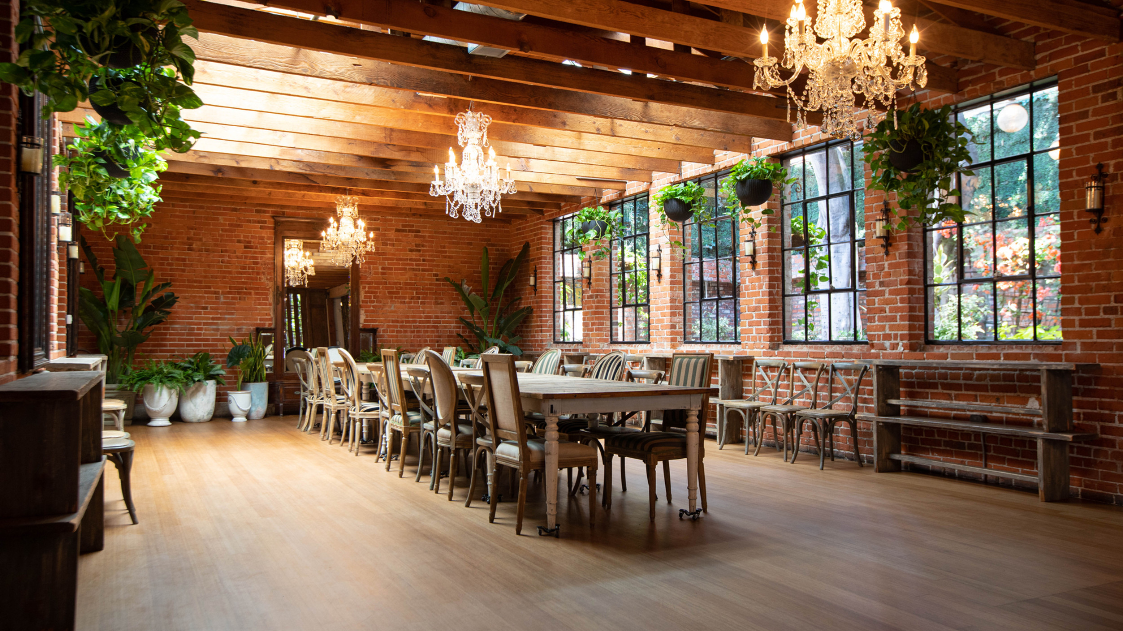 Carondelet House - Bronson Hospitality A charming indoor event space at Carondelet House featuring exposed brick walls, crystal chandeliers, natural greenery, and a warm rustic-industrial atmosphere