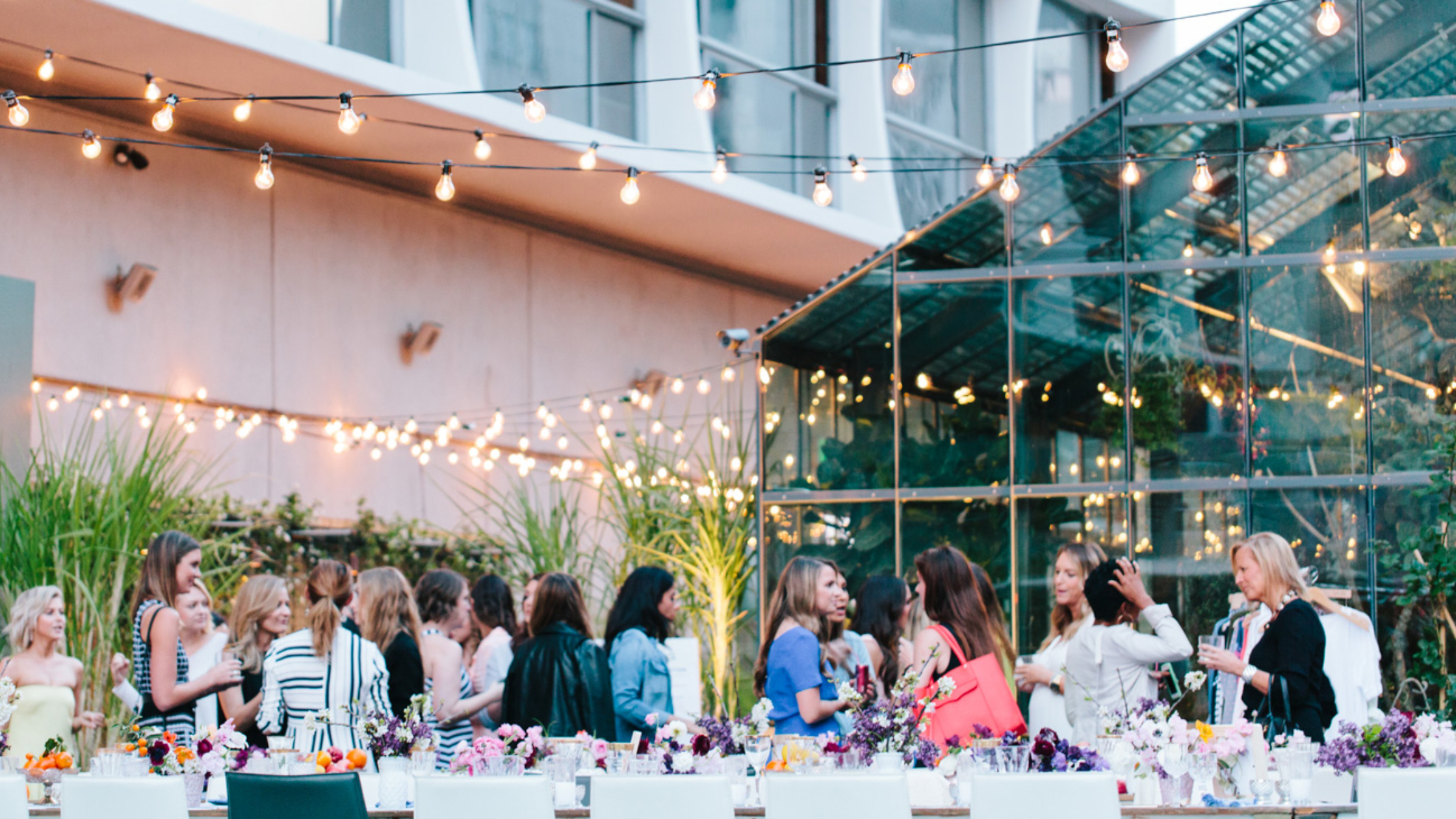Openaire - Bronson Hospitality "A stylish outdoor event space at Openaire featuring string lights, lush greenery, modern glass architecture, and an elegant social gathering atmosphere