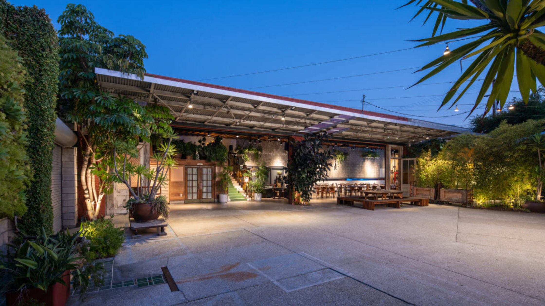 SmogShoppe - Bronson Hospitality "A modern outdoor event space at SmogShoppe featuring lush greenery, warm ambient lighting, and an industrial-chic setting with a stylish open courtyard atmosphere
