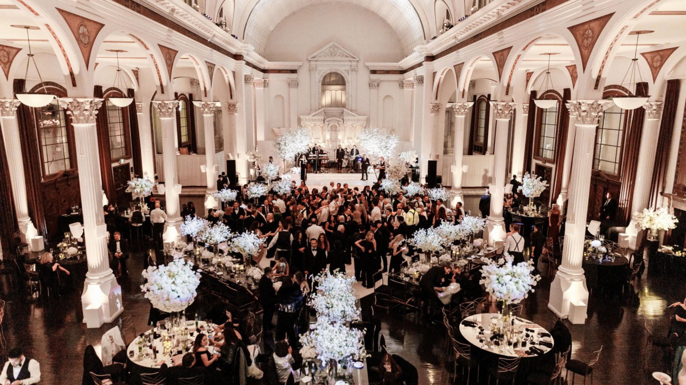 Vibiana - Bronson Hospitality An elegant grand ballroom at Vibiana LA featuring soaring ceilings, dramatic columns, luxurious floral arrangements, and a lively reception atmosphere with sophisticated event décor.