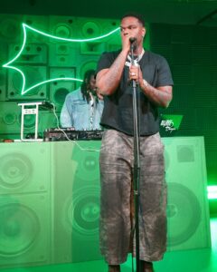 Sprite-casita-hollywood-brand-event - Bronson Hospitality Male performer sings into a microphone on a neon-green stage, DJ at equipment in the background.
