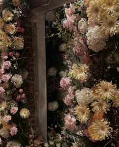 SnapInstato_687541964_17998567556930224_2399216660517196876_n - Bronson Hospitality Pastel floral arch framing a doorway with cream, pink, and pale yellow blooms (roses, dahlias, hydrangeas).